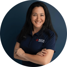 Professional headshot of Alissa D in branded attire, smiling with arms crossed, dark background.