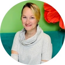 Professional headshot of Christina G in a light sweater, smiling with a green background.